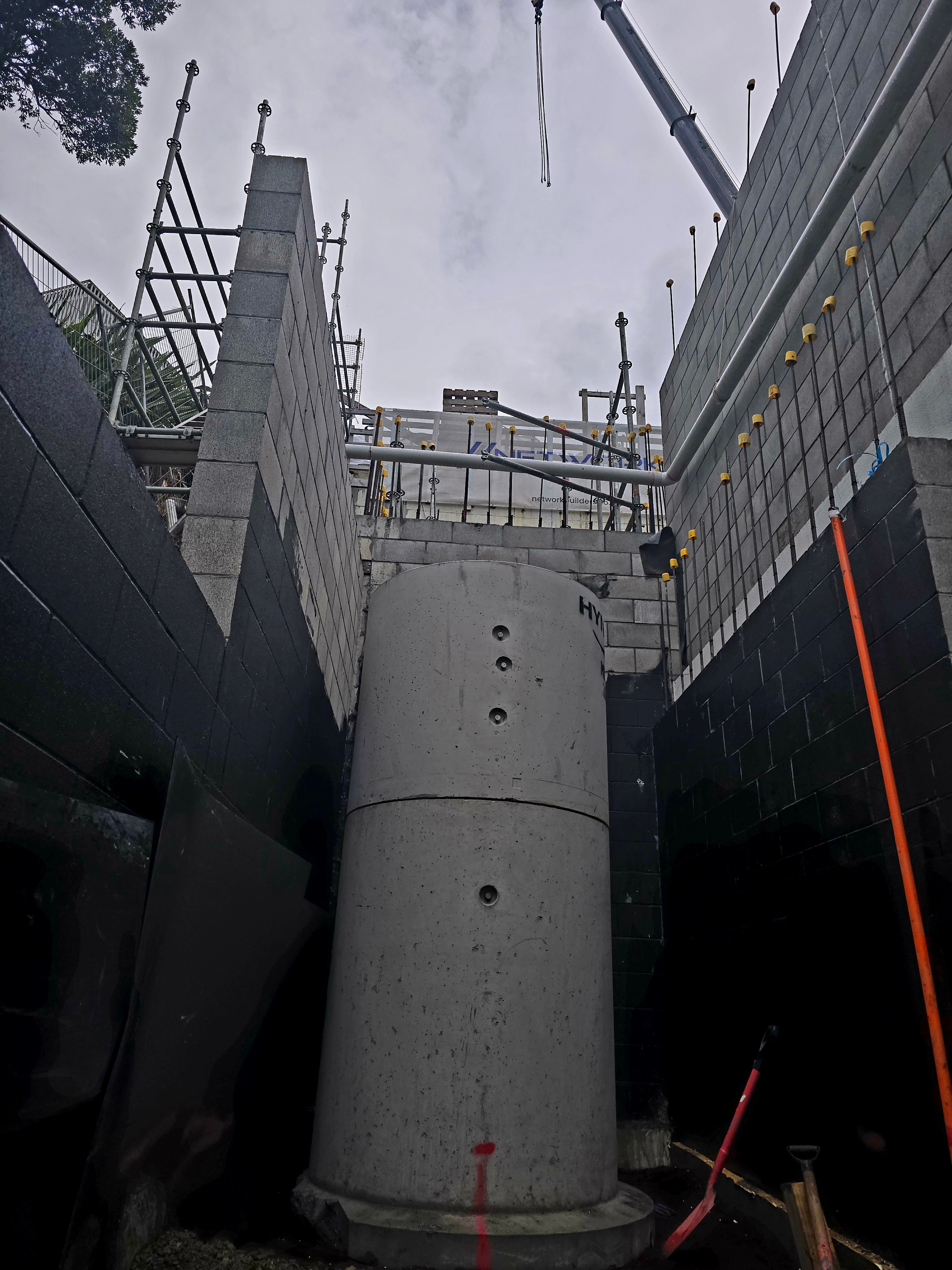 Concrete manhole riser standing between blockwork walls with a crane boom overhead