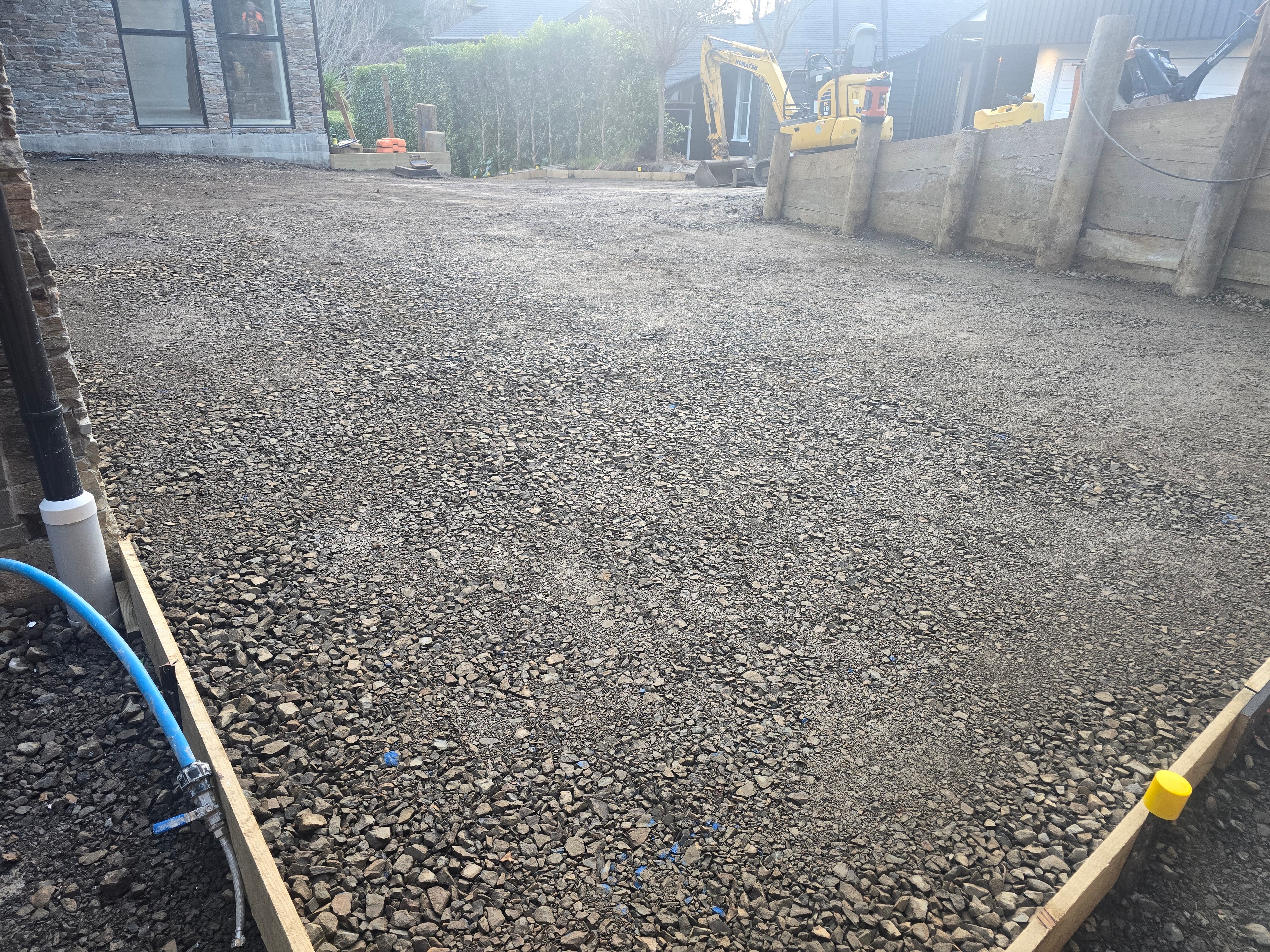 Excavator parked on a completed basecourse driveway beside a timber retaining wall