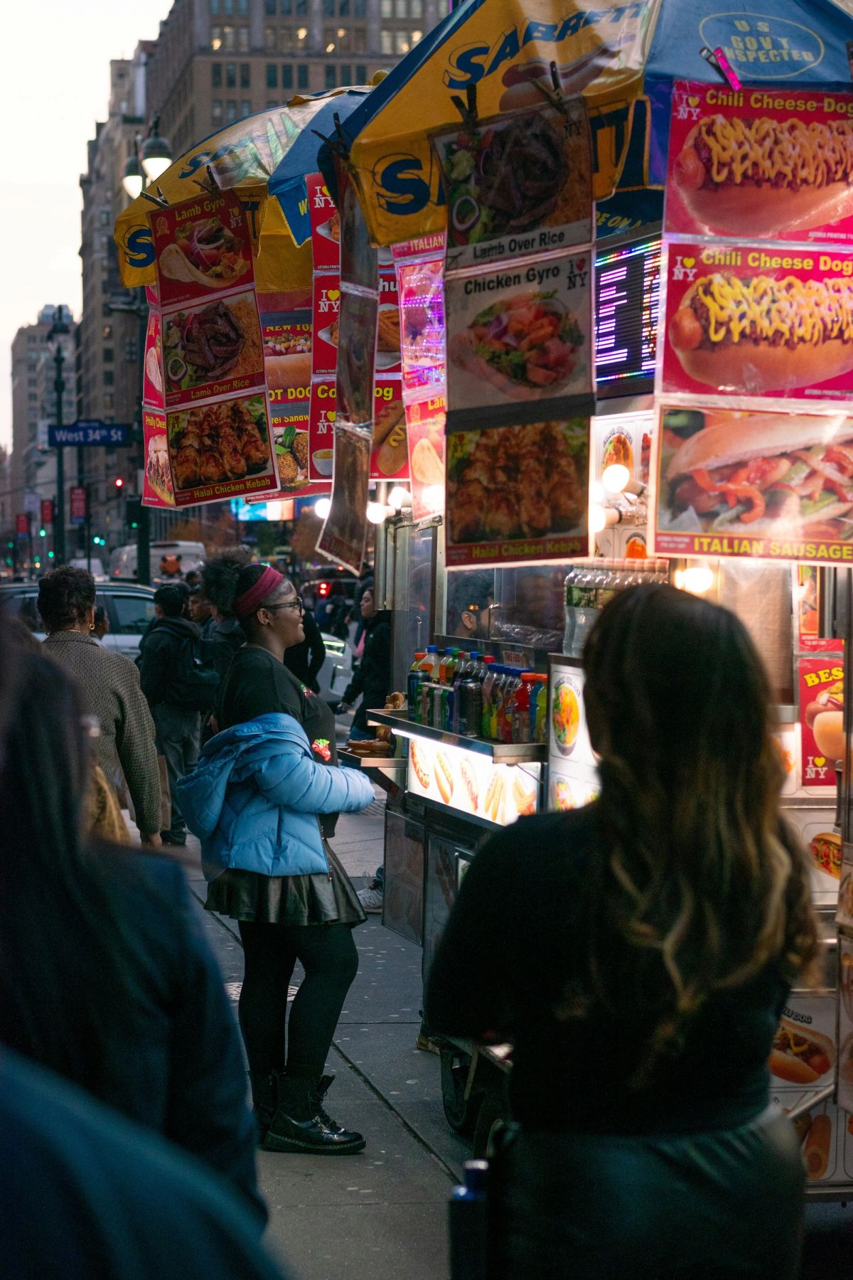 A crowd queuing at a food cart on West 34th Street covered in menu photos