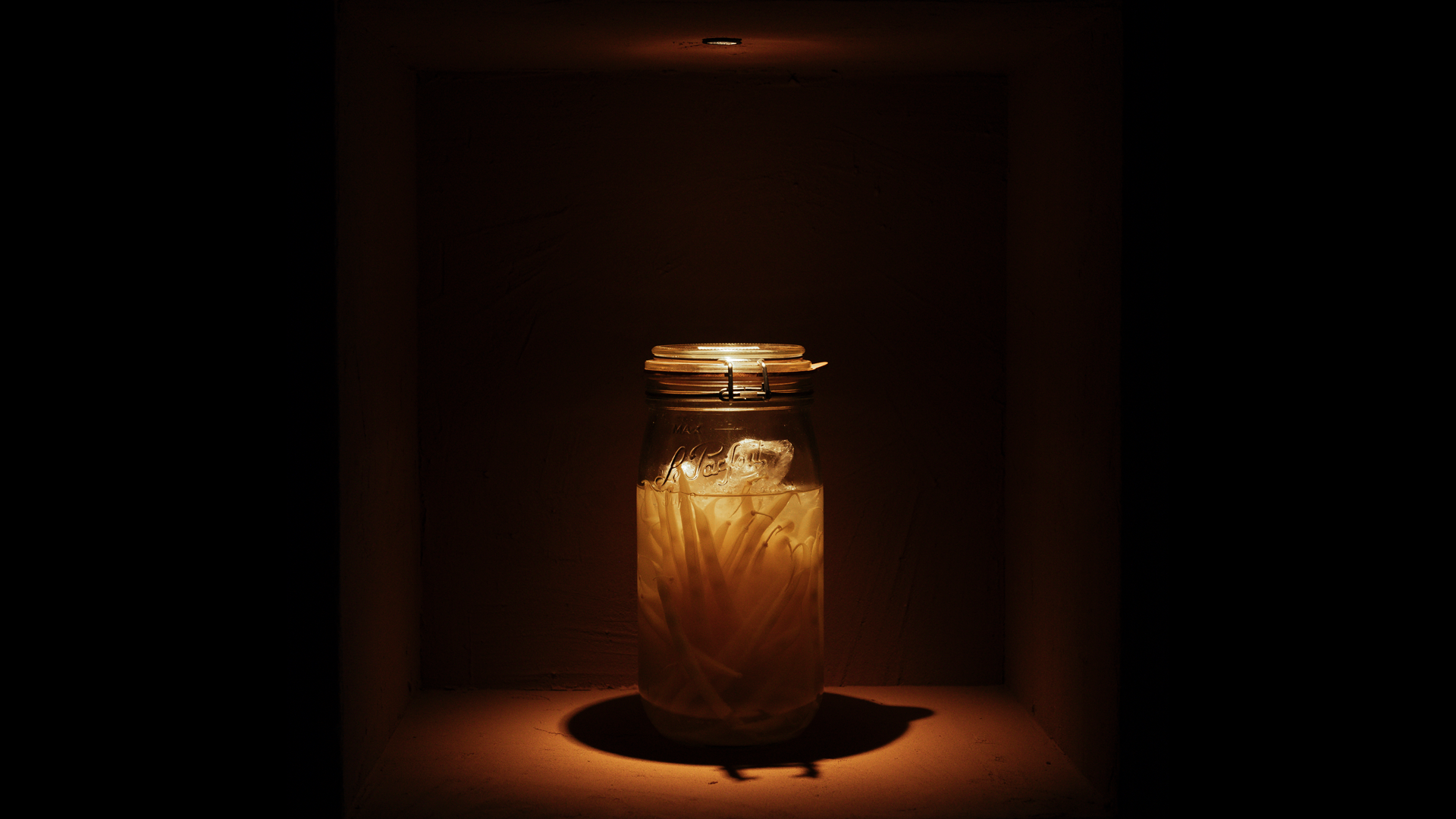 Een glazen pot met paddenstoelen, vijgen en kruiden, ingelegd in amberkleurige vloeistof.