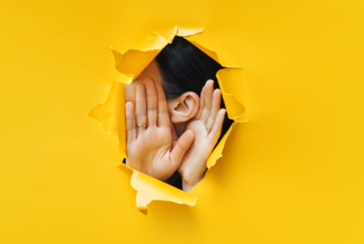 Gizli işitme kaybını temsil eden, sarı arka plan üzerinden kulağını dinlemeye çalışan kişi görseli.