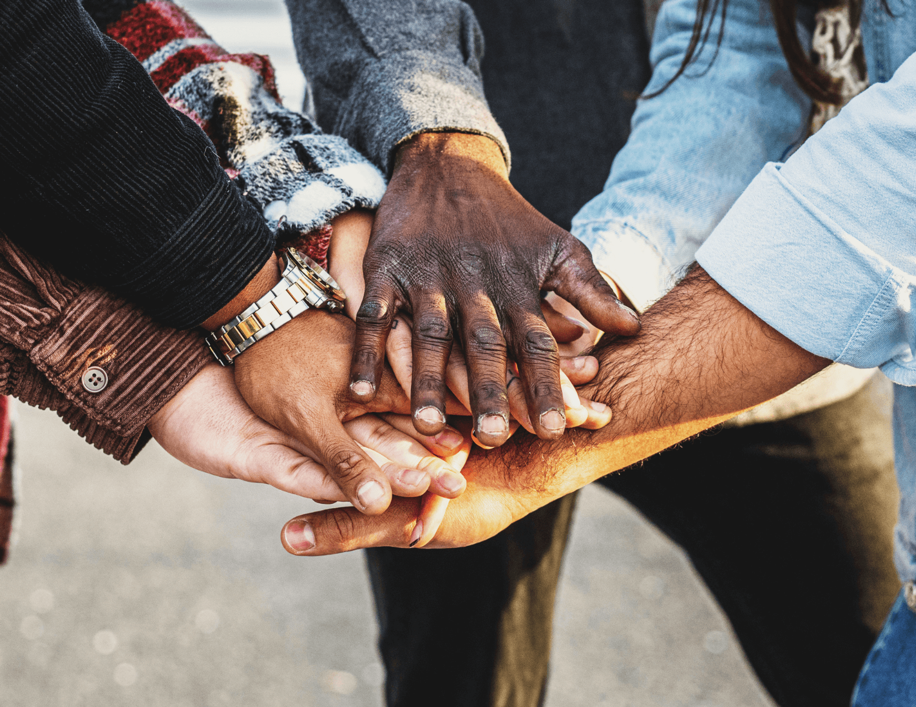 Several people from various backgrounds, gathered in a circle with hands together in the middle.