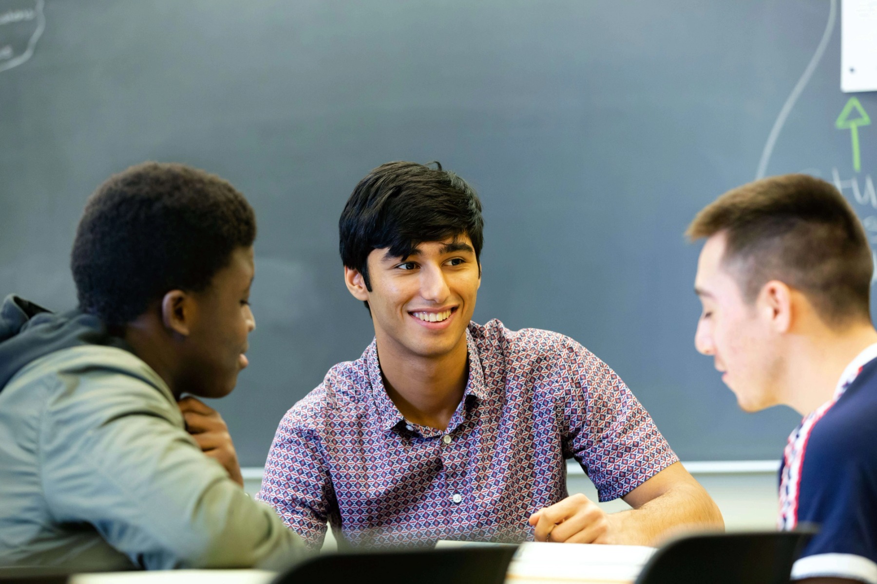 Three young men of diverse backgrounds sitting together in a classroom.