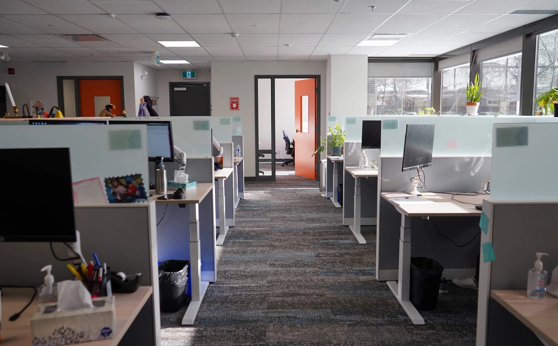 Rows of office desks on either side, with an open office door at the end of the corridor.