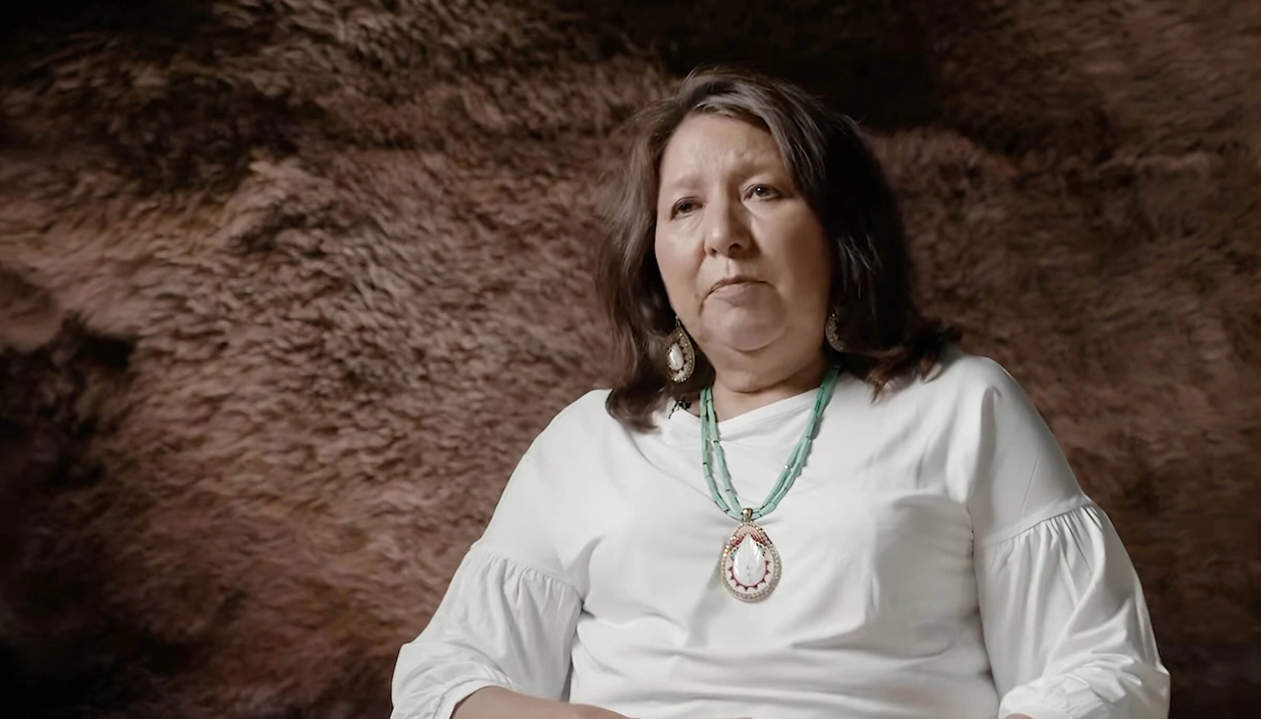 A woman in a white shirt and necklace, being interviewed about land acknowledgement
