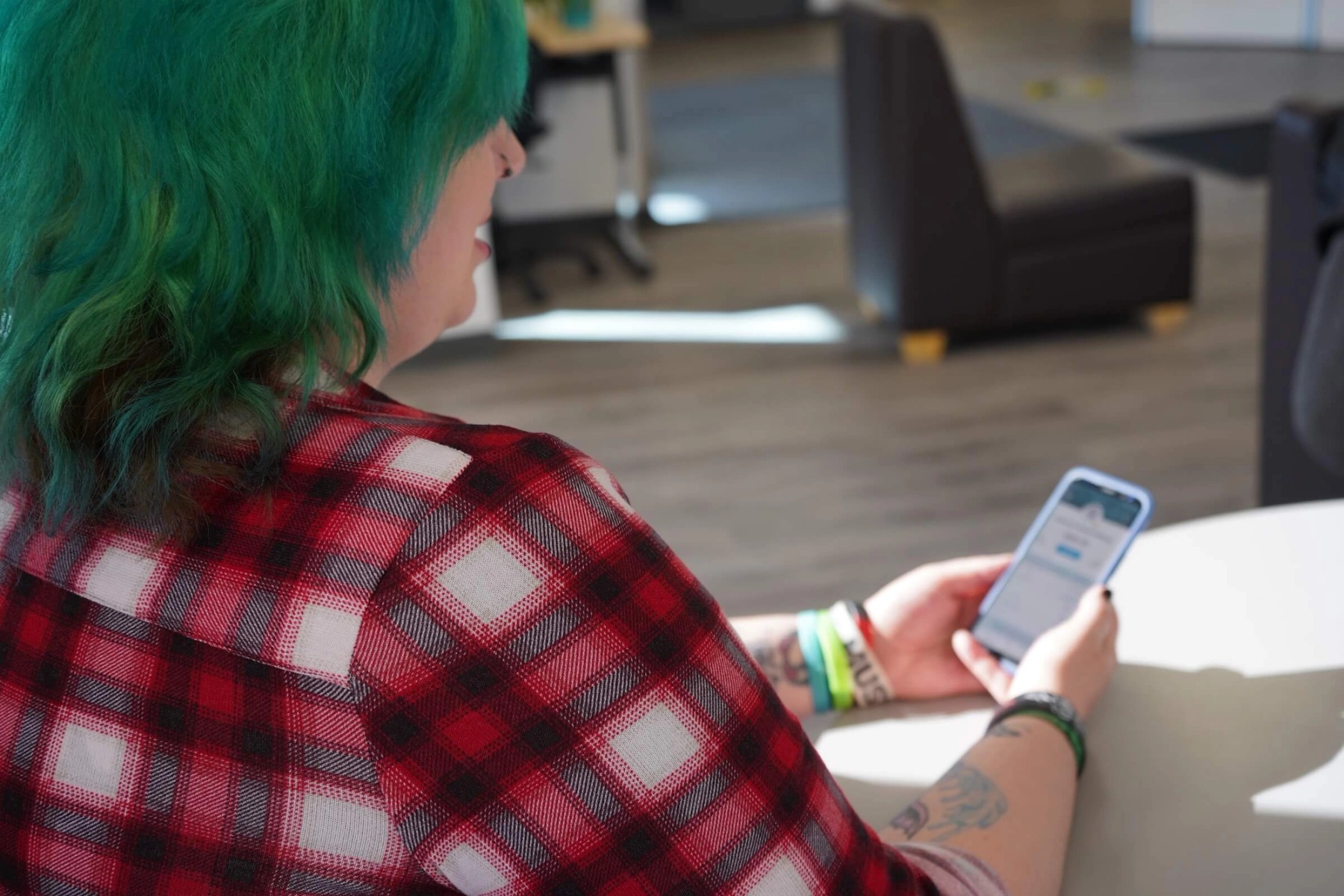 A person with long green hair and a red plaid shirt uses an app on their phone.