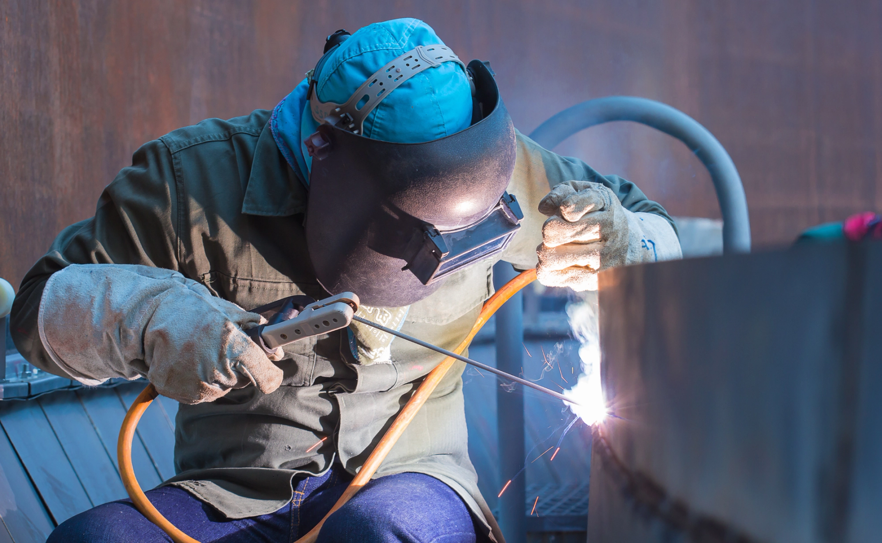 A person wearing a welding mask and PPE, welding at their job site.