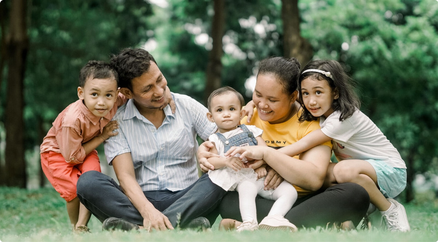 A family of five sits in the grass and smiles for a photographer.
