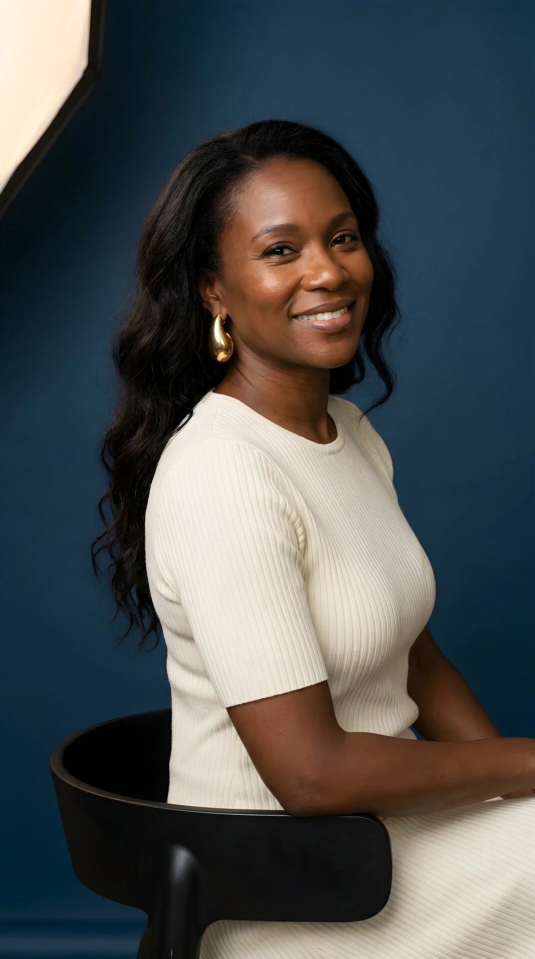 Portrait of a woman seated and smiling naturally against a Prime Blue background — representing skin and body confidence after GLP-1.