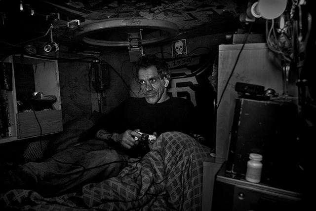 Tate playing a video game in his box, which was part of the homeless encampment at the corner of Harrison and Division, February 21, 2016 (by Robert Gumpert, Harper's Magazine).