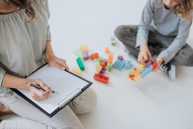 Una profesional toma notas mientras un niño juega con bloques de colores