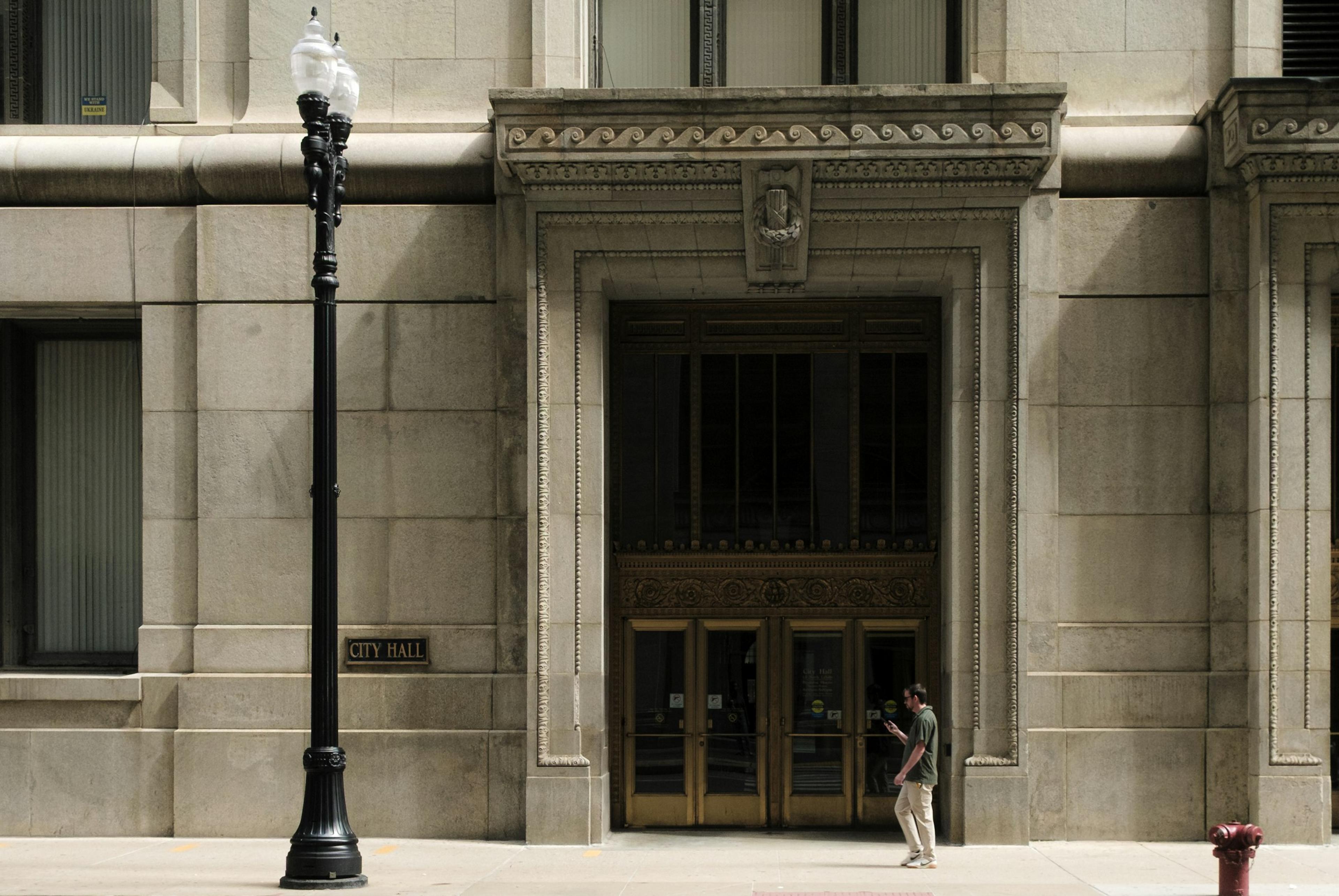 A person walking past an ornate building entrance and street lamp