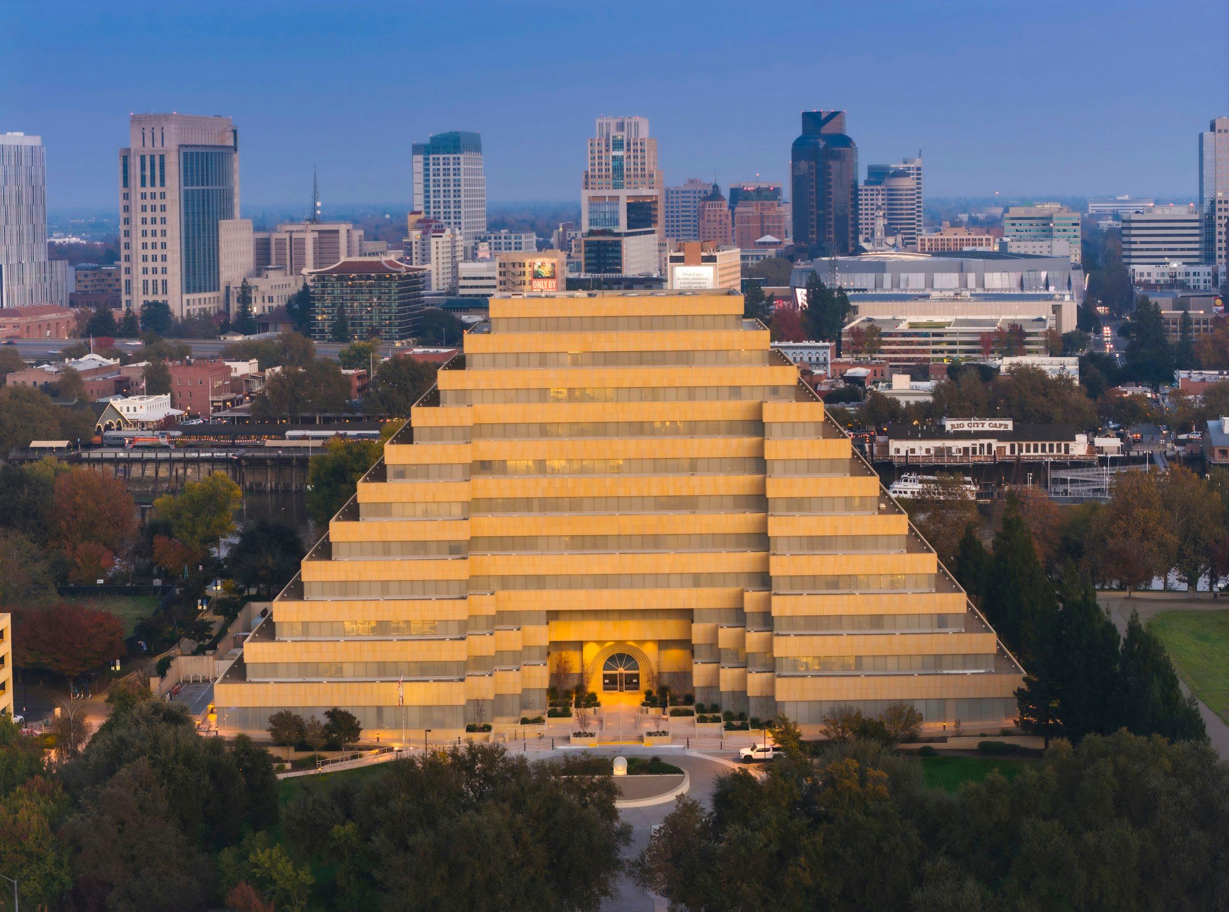 A pyramid-form building in a city skyline at dusk