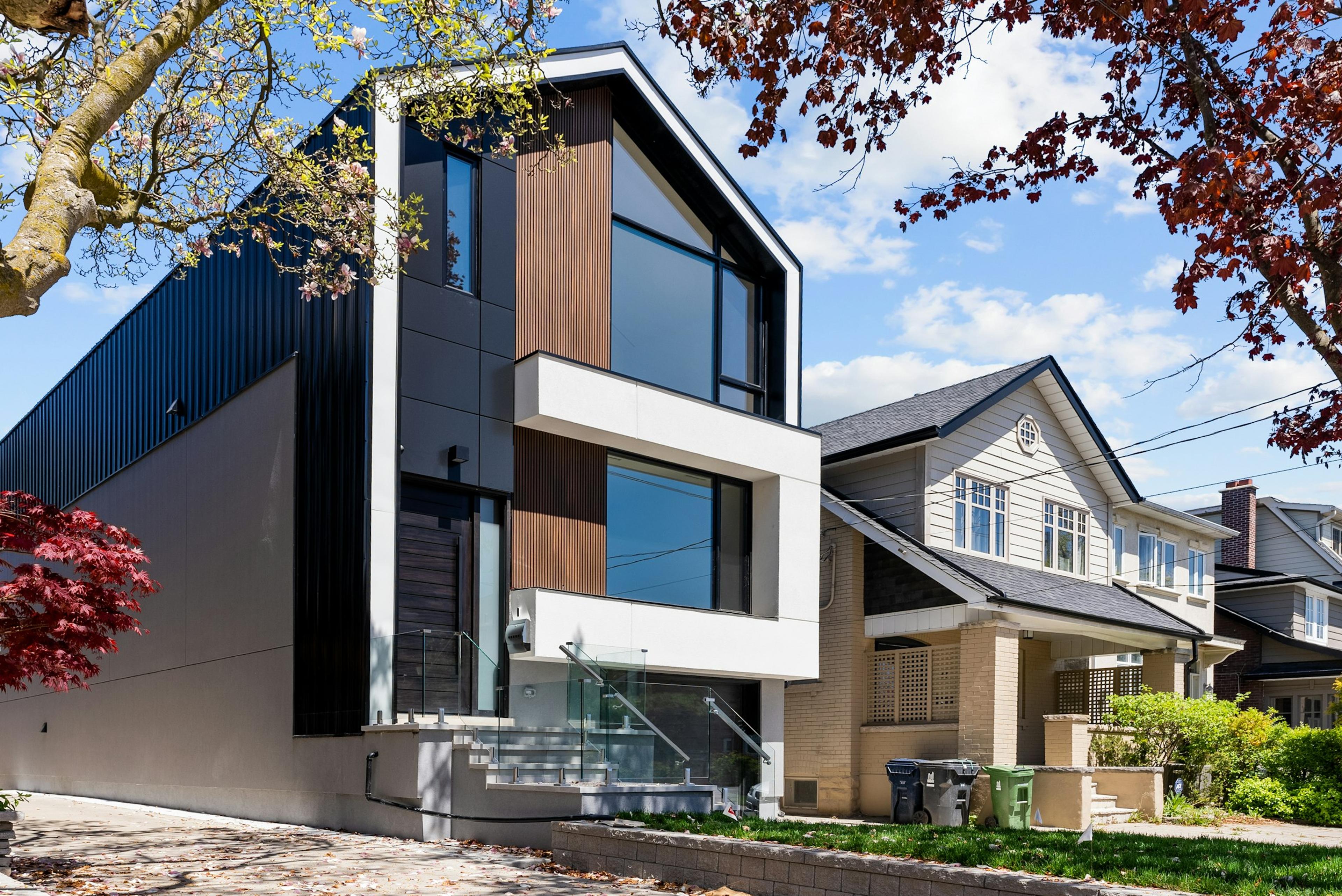 A modern house clad in black metal beside a traditional house