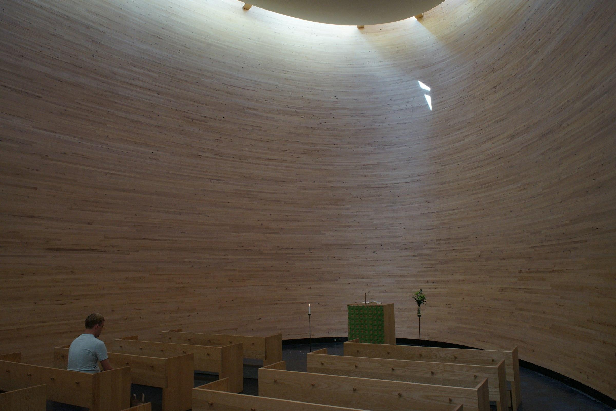 A timber chapel interior with light rays and a single figure