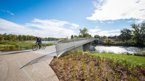 A photography of a cyclist crossing the Elbow River Traverse pedestrian bridge
