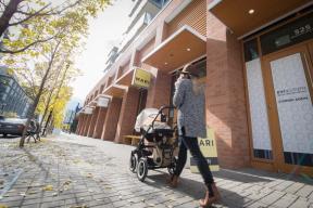 A photograph of a woman with a stroller walking down a brick paved sidewalk in East Village.