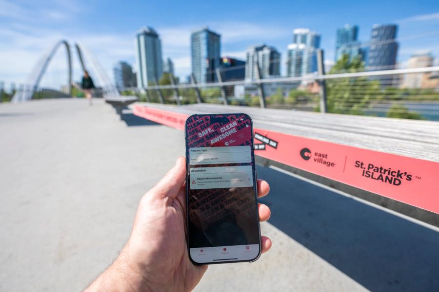 A photo of the Safe, Clean and Awesome App on a phone with East Village skyline in the backdrop