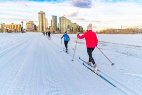 A photograph of people skiing on Nordic Loop with the Calgary skyline and Calgary Tower in the background