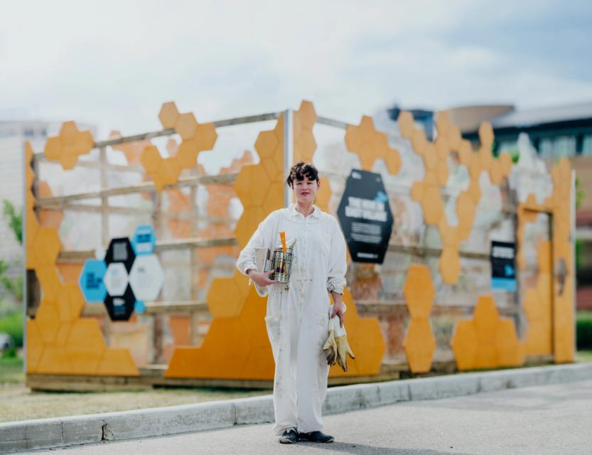 A photograph of a bee keeper standing outside the Hive