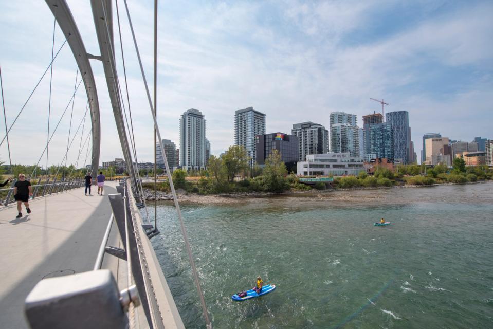A photograph of the East Village skyline from the George C. King bridge with the Bow River and people on paddleboards