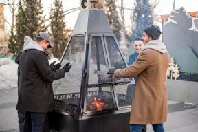 A photograph of 4 people warming their hands at the Hygge Hut firepit