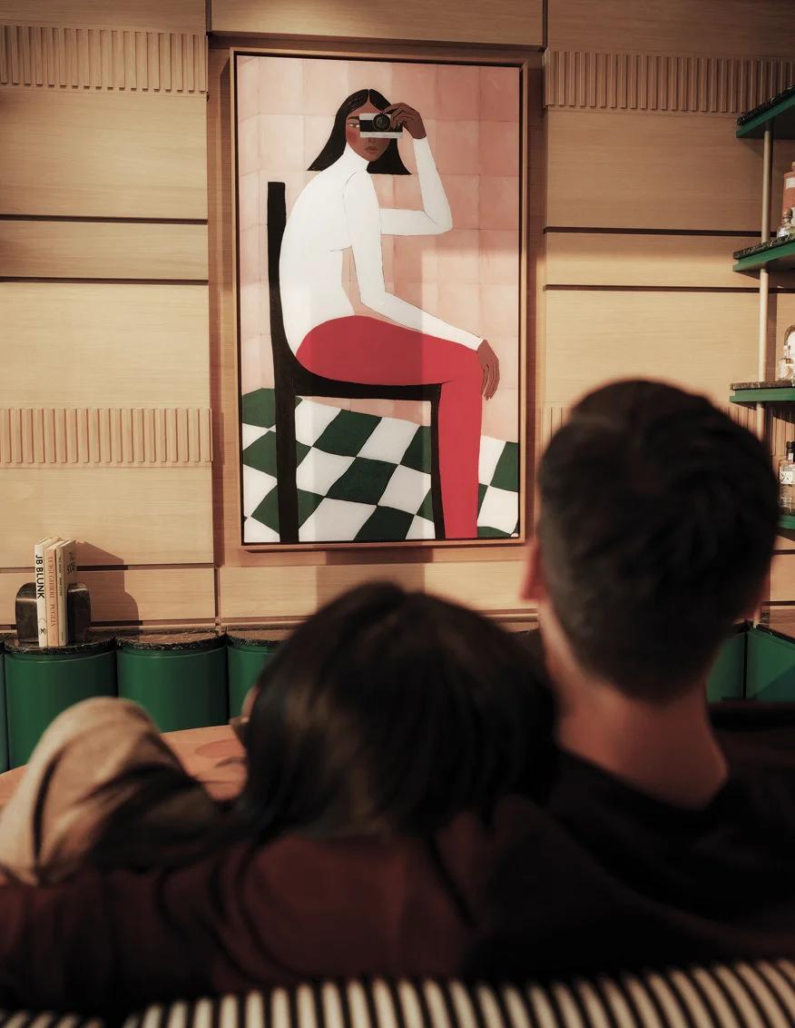 Couple on a green banquette below a figurative painting