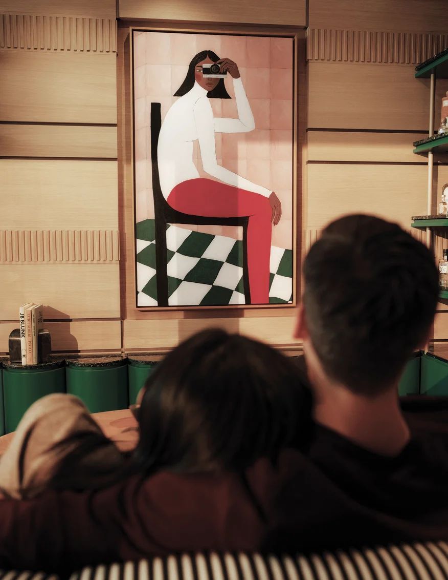 Couple on a green banquette below a figurative painting