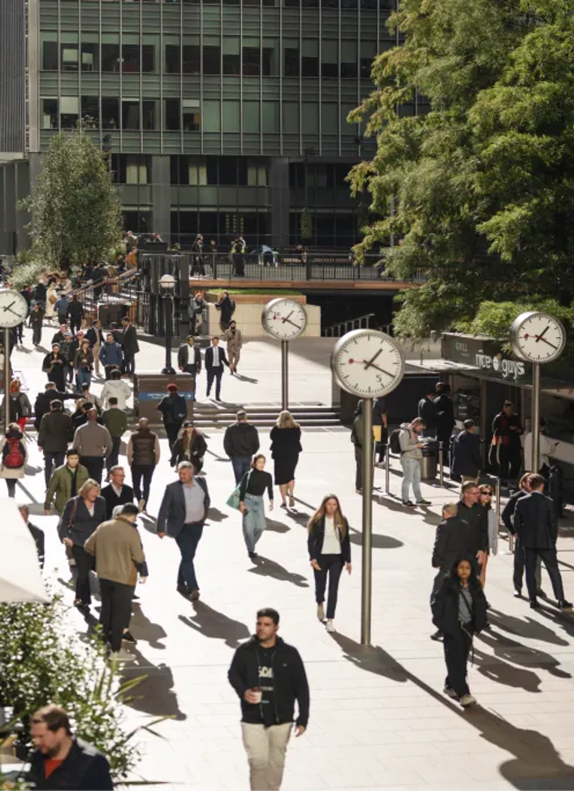 Crowds crossing a plaza past its row of clocks