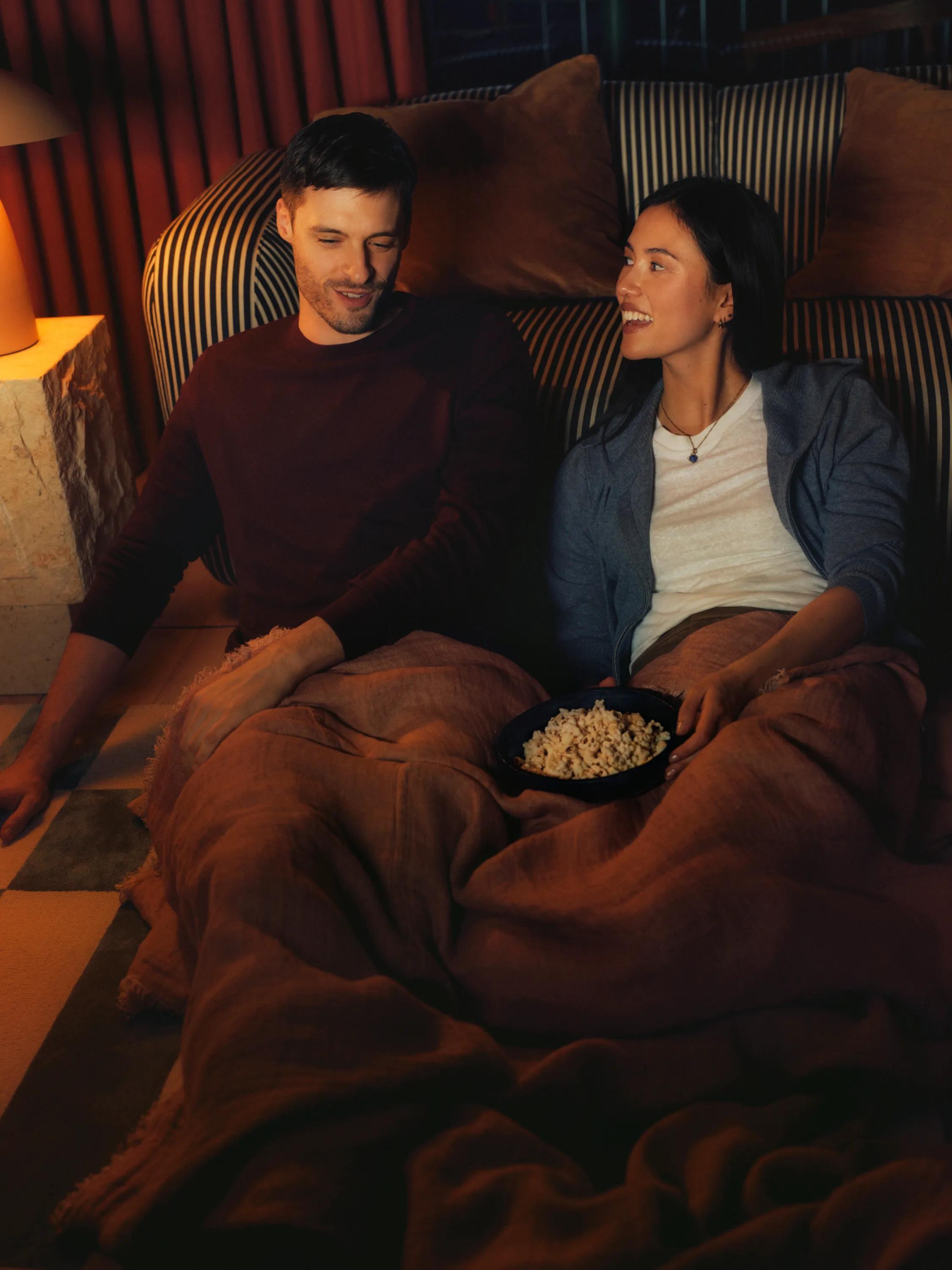 Two residents under a blanket with popcorn, watching a film