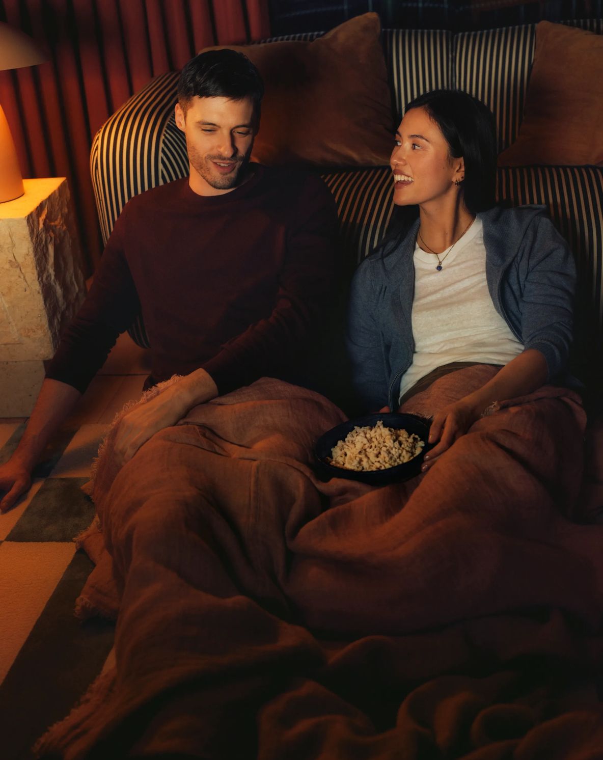 Two residents under a blanket with popcorn, watching a film
