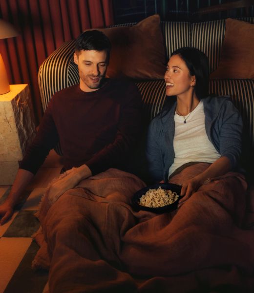 Two residents under a blanket with popcorn, watching a film