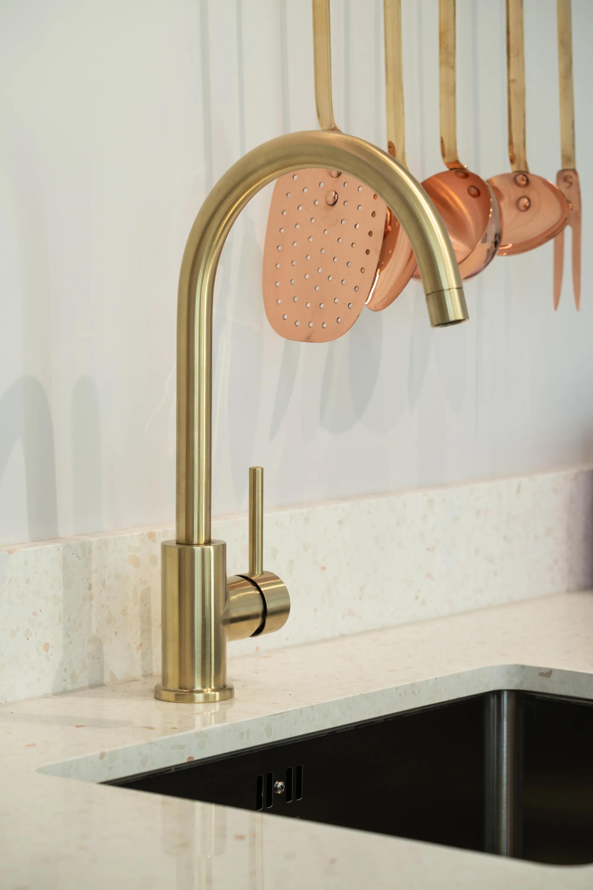Brass tap over an undermount sink with copper pans above