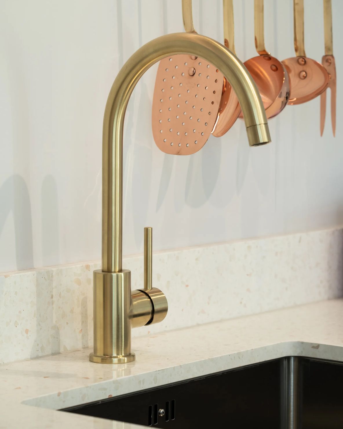 Brass tap over an undermount sink with copper pans above