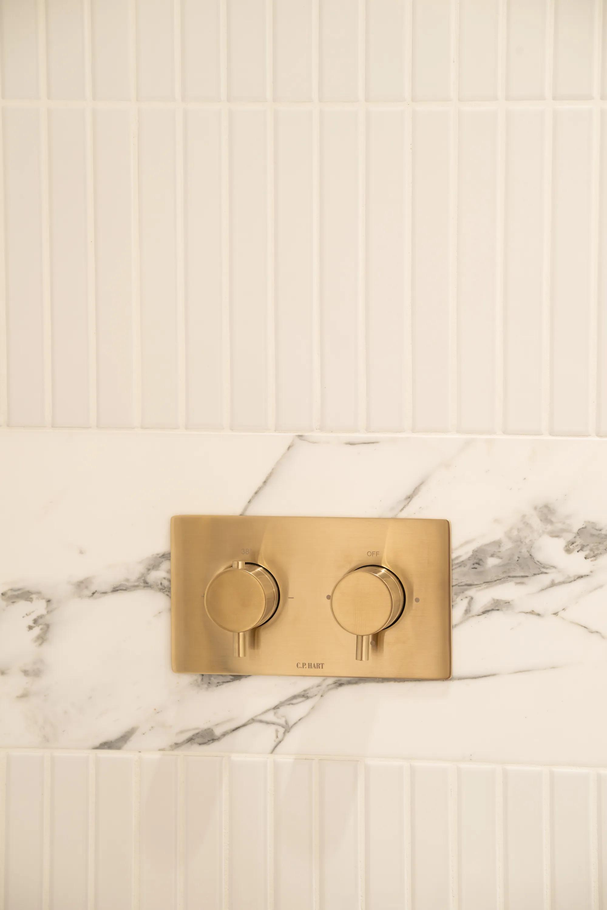 Brushed brass shower controls on marble and white tiling