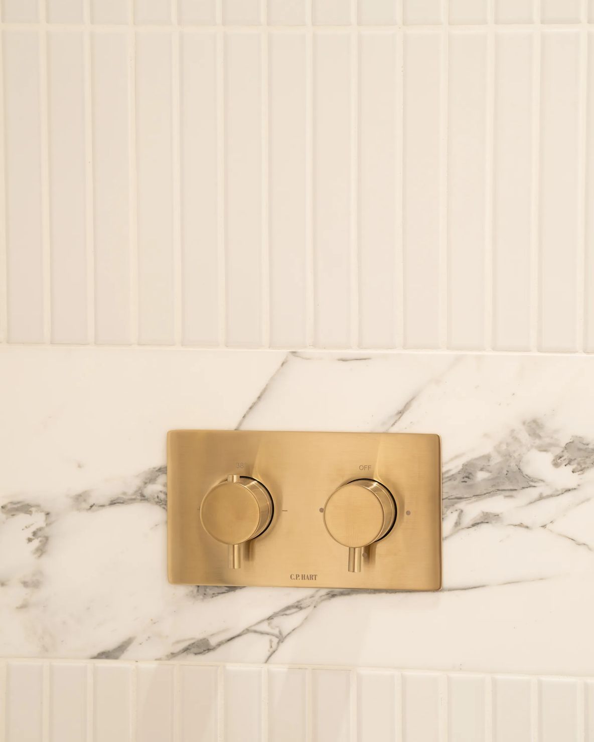 Brushed brass shower controls on marble and white tiling