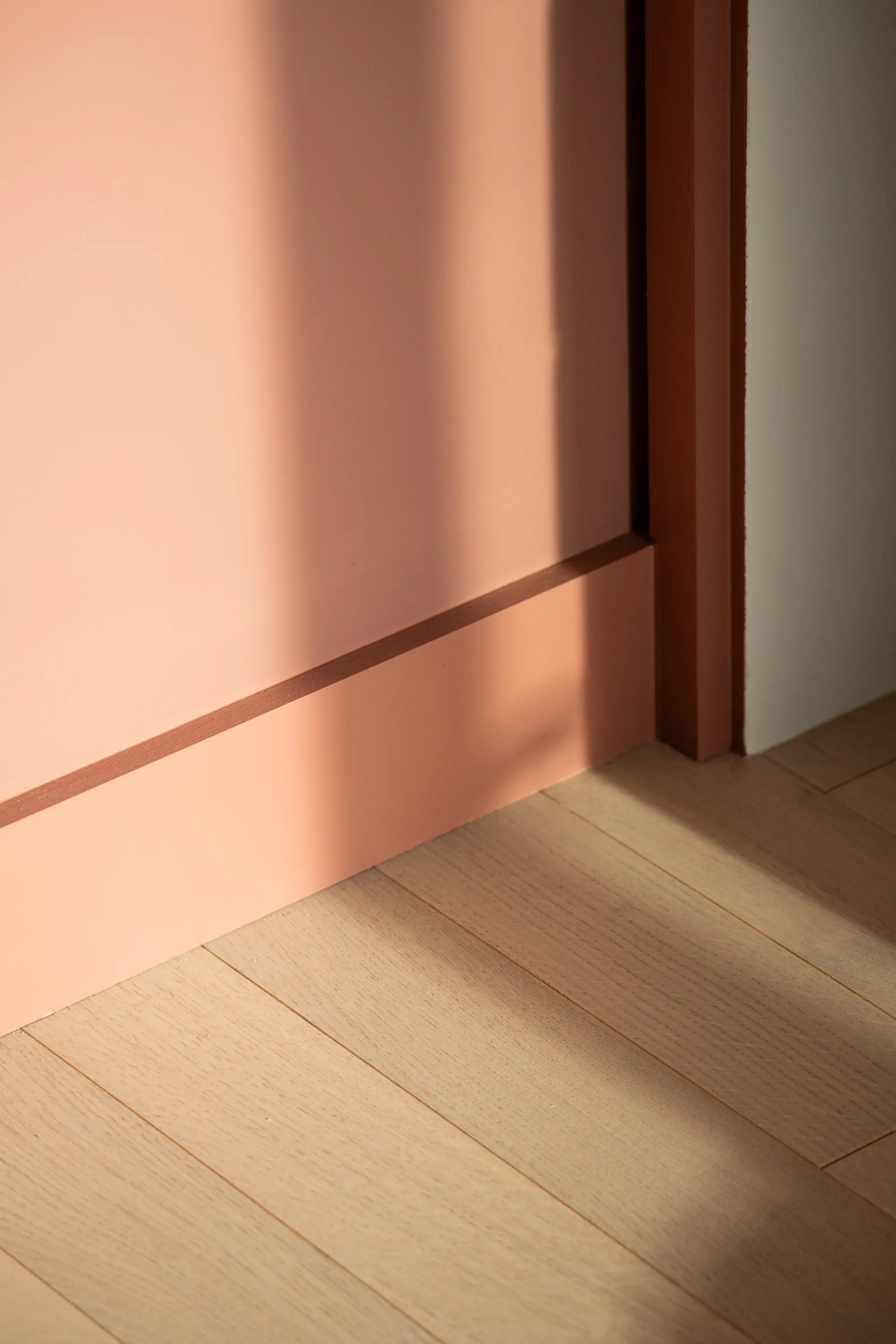Coral painted wall meeting a timber reveal and oak floor