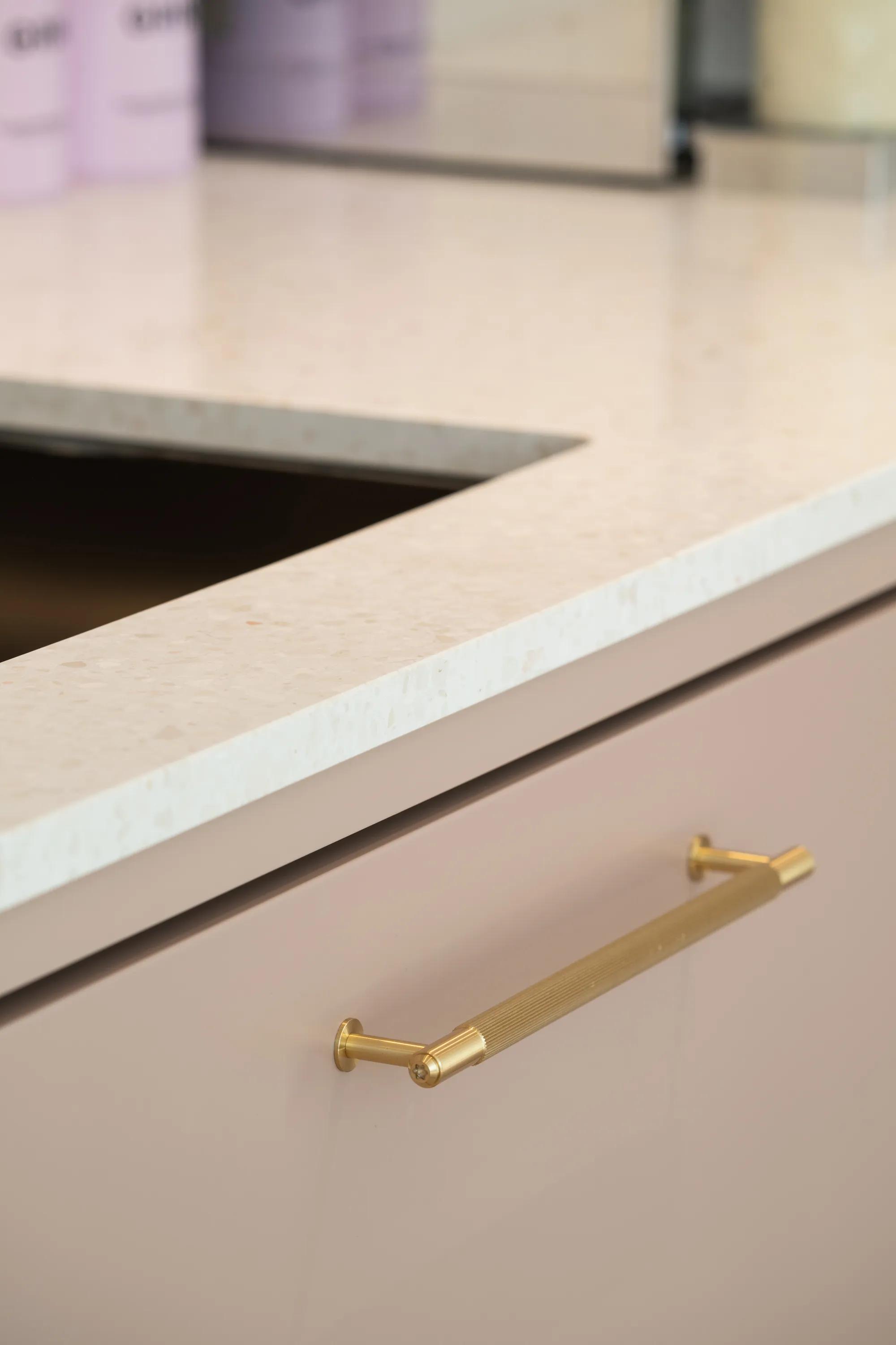Blush cabinet front with a slim brass handle under stone worktop