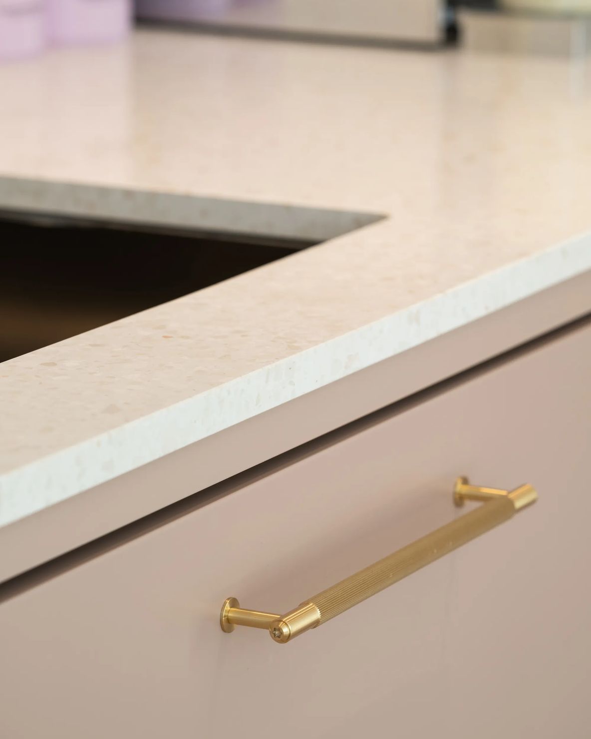 Blush cabinet front with a slim brass handle under stone worktop