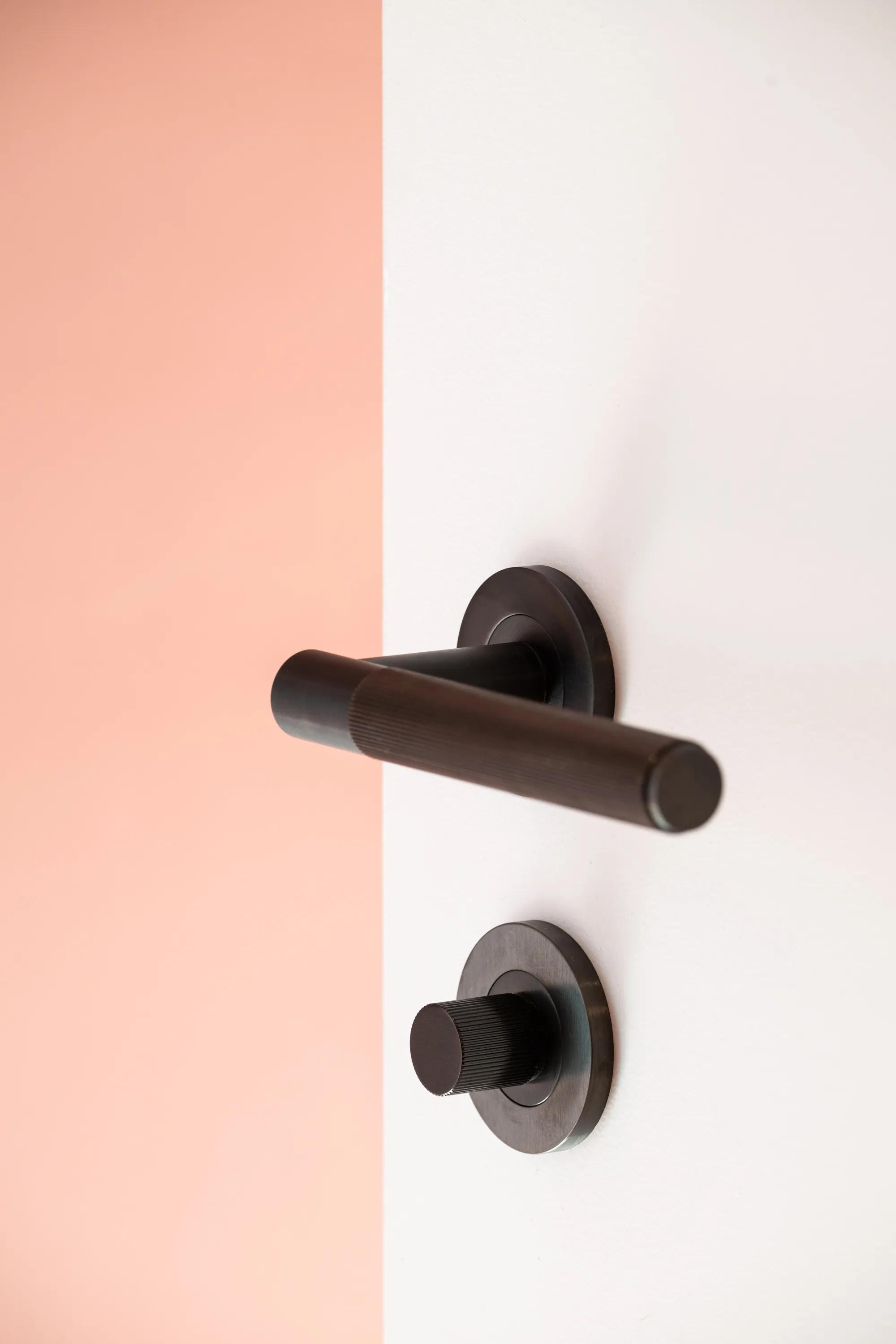 Bronze lever handle on a white door beside a coral wall
