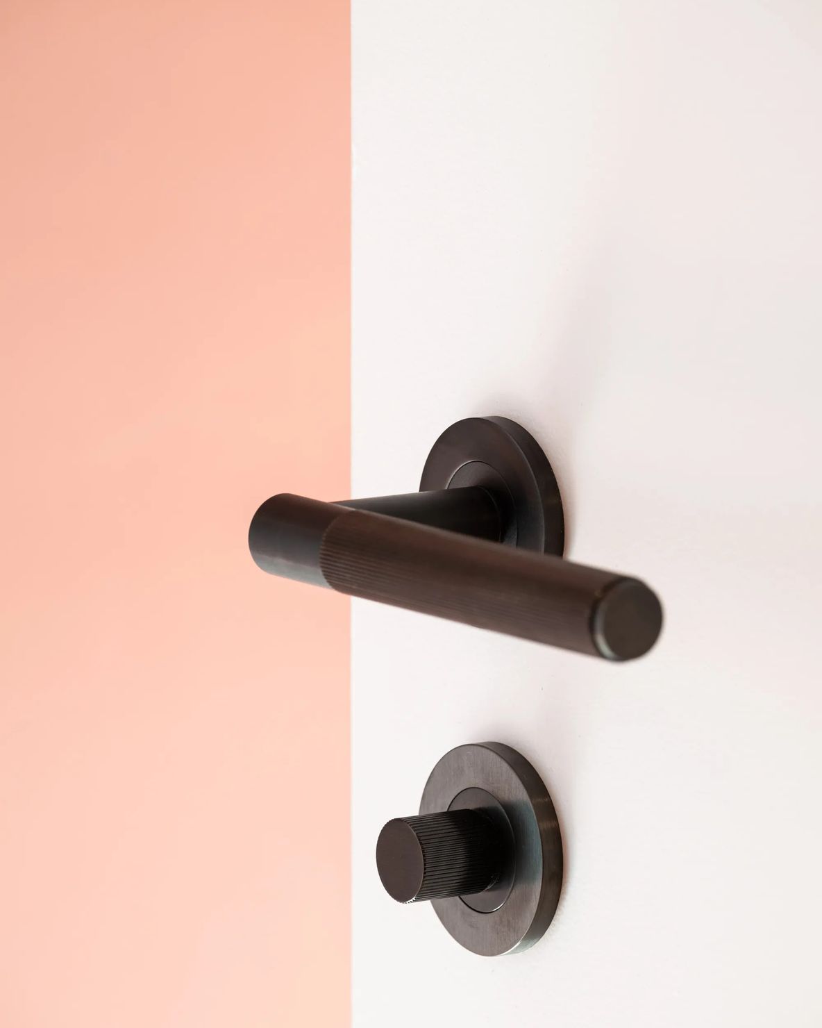 Bronze lever handle on a white door beside a coral wall