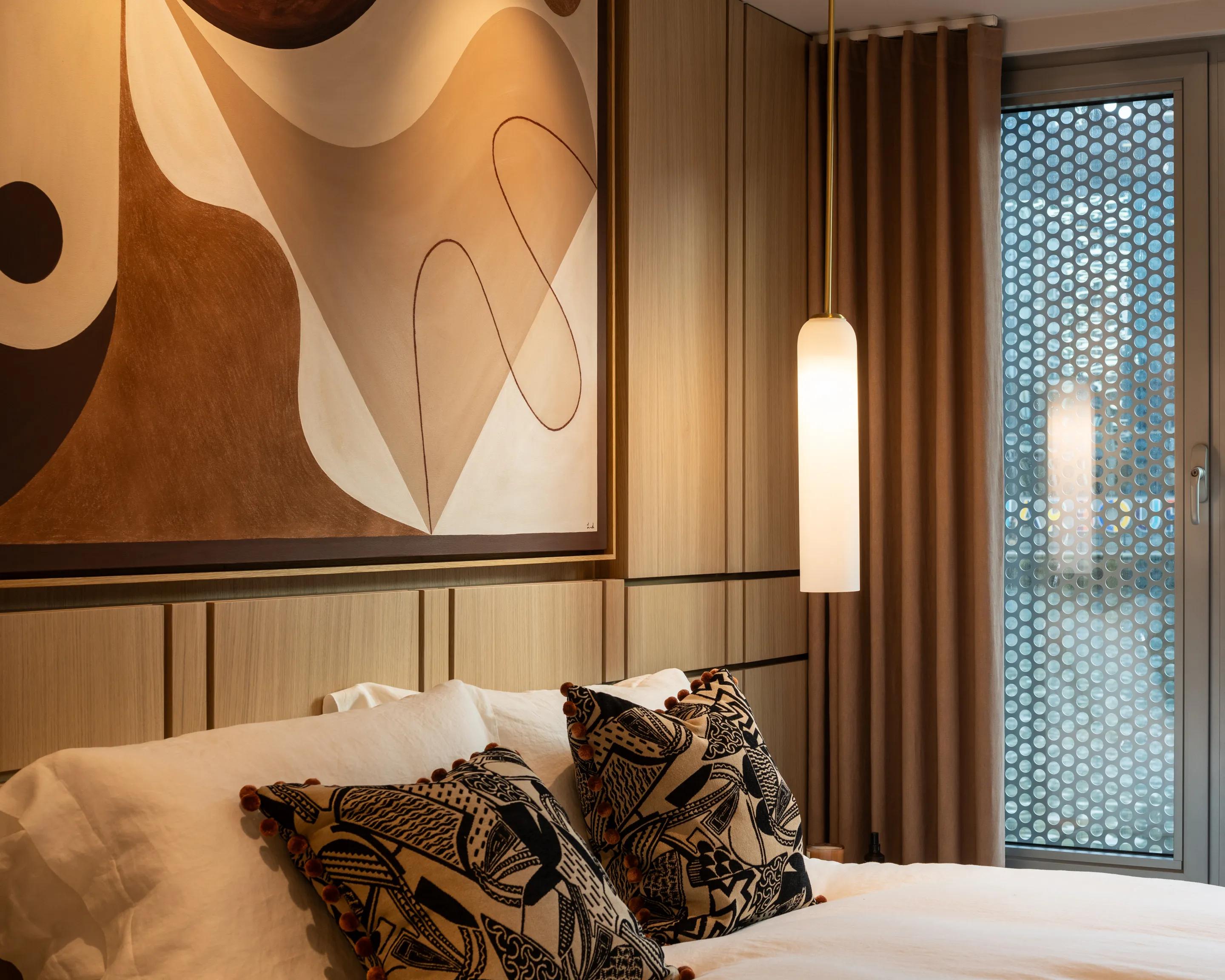 An apartment bedroom, artwork above the bed and a pendant light alongside
