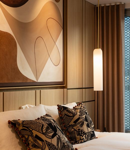 An apartment bedroom, artwork above the bed and a pendant light alongside