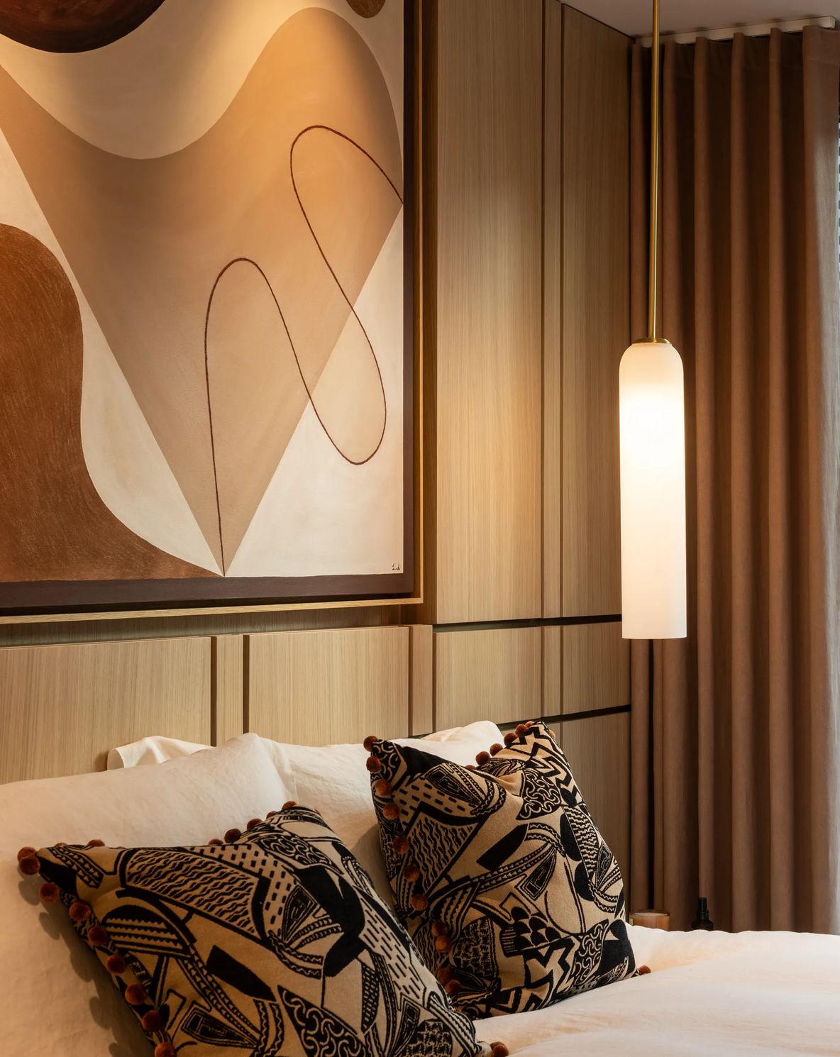 An apartment bedroom, artwork above the bed and a pendant light alongside