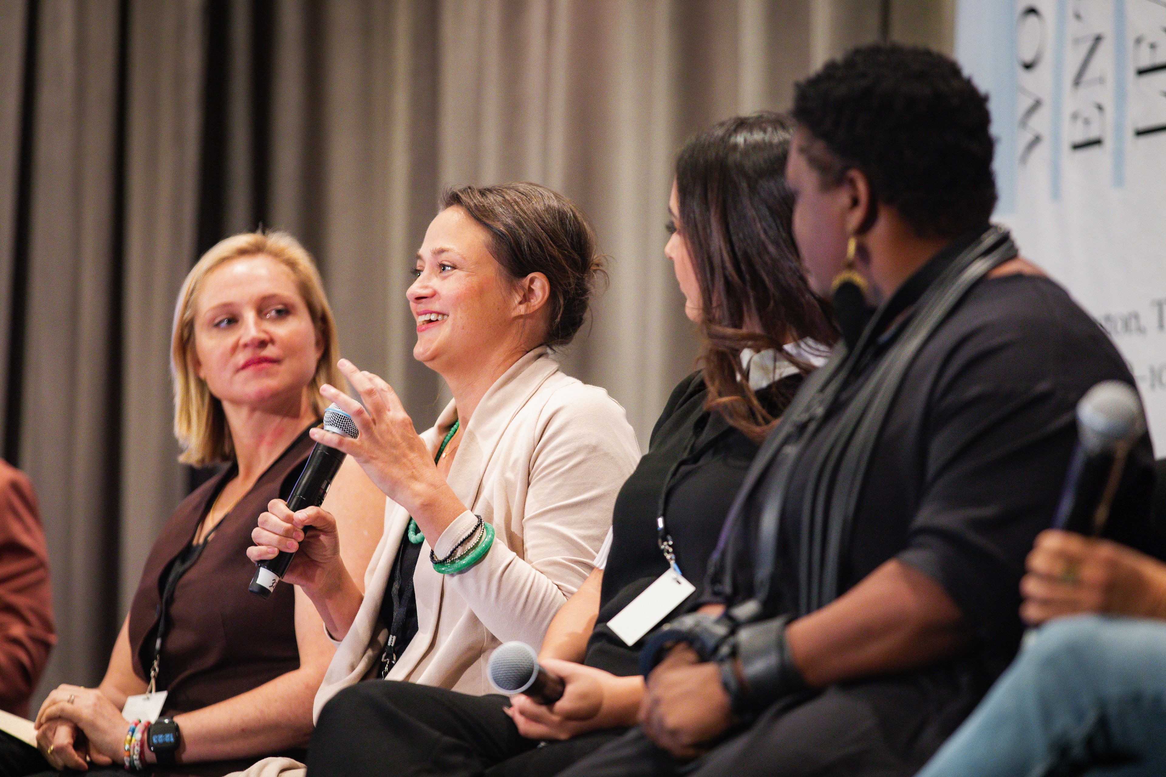 Women sitting on stage with microphones at a panel