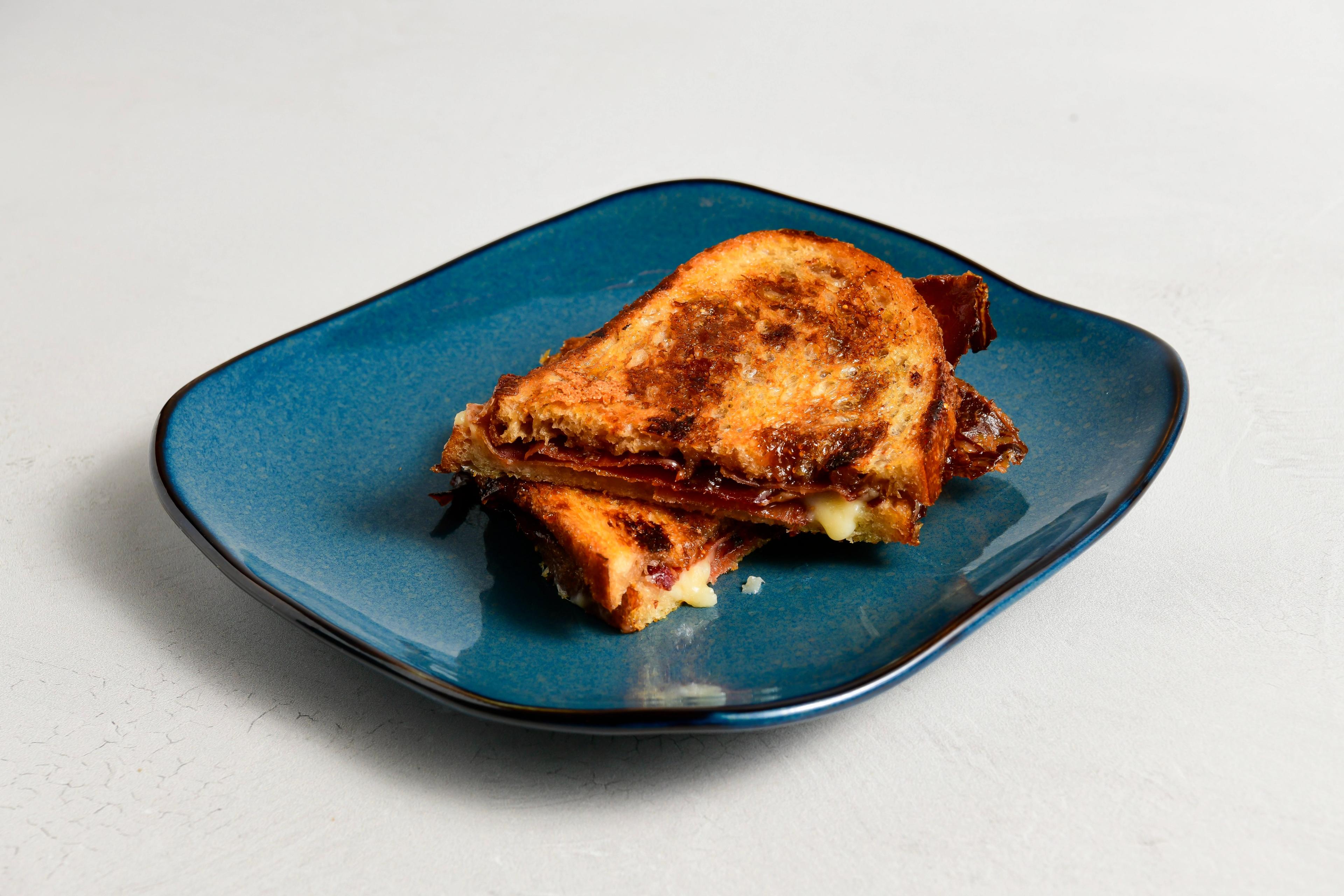 A grilled cheese with speck, goat cheese, and fig on a blue plate