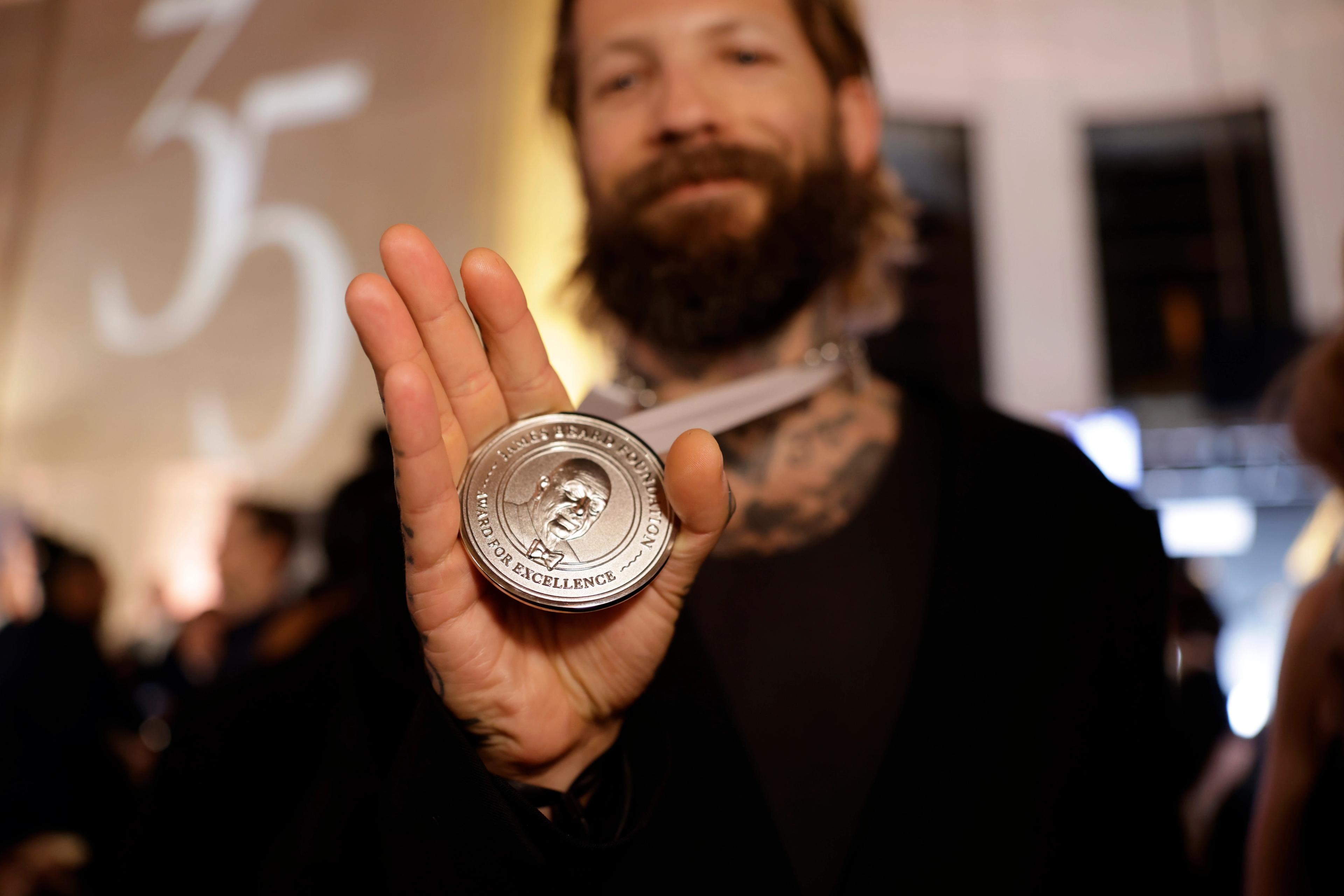 Man holds out a 2025 James Beard Award medallion
