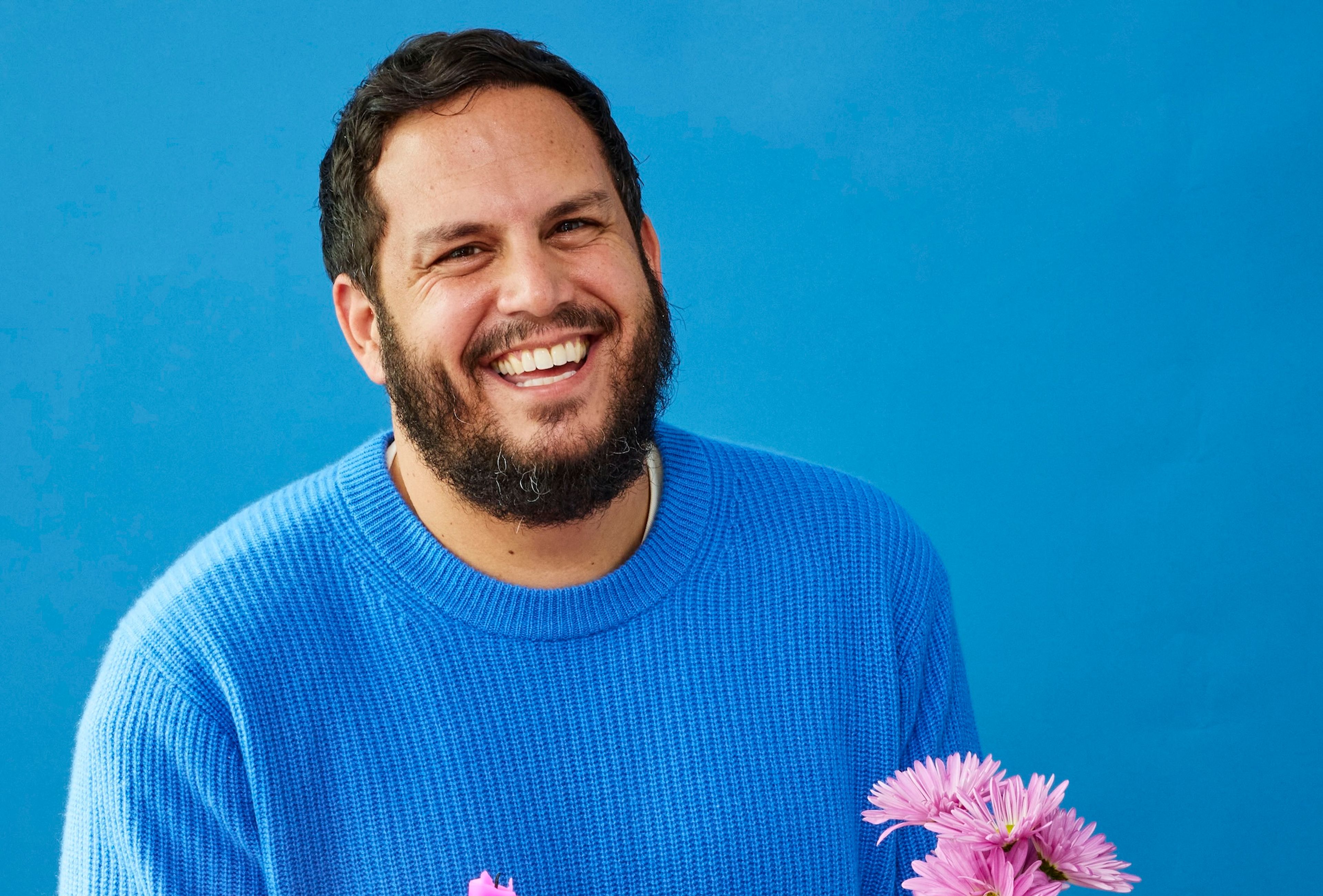 Chef Dan Pelosi smiles and holds a tray with rolls, dip, plates, flowers, and other tablescape objects