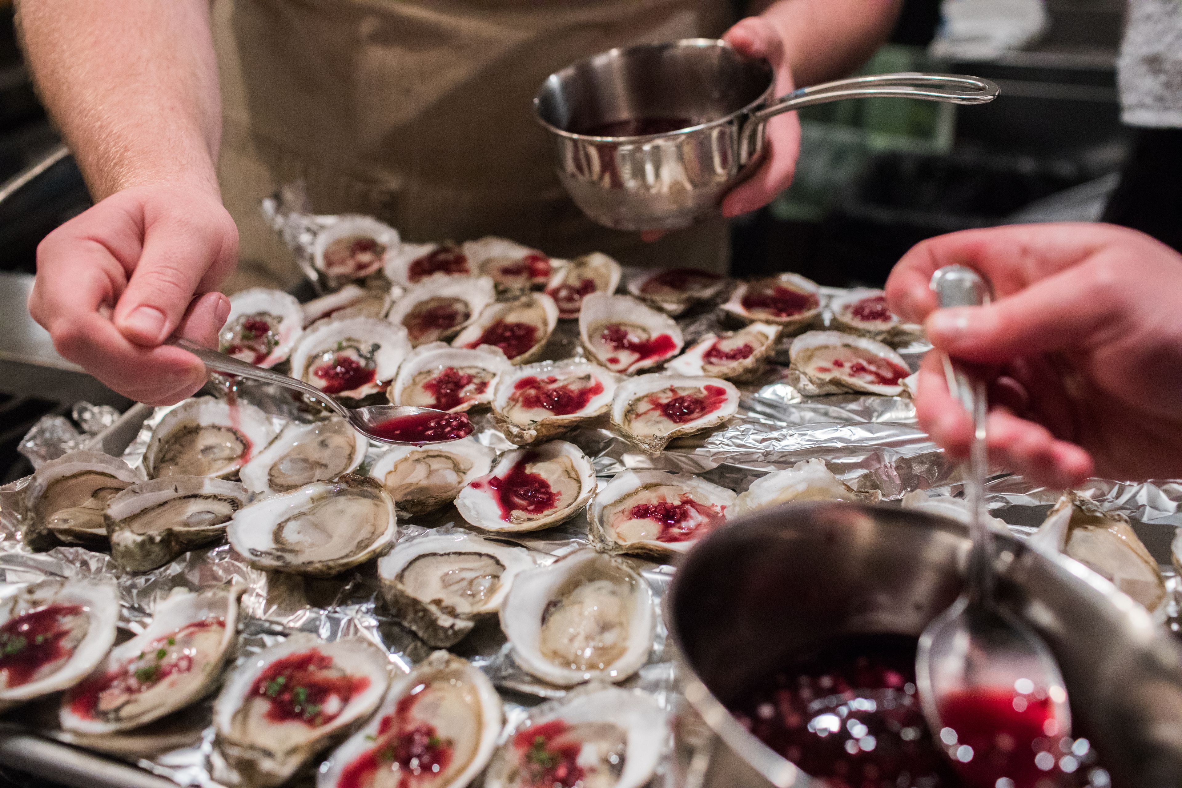 Hands adding a red mignonette on top of oysters