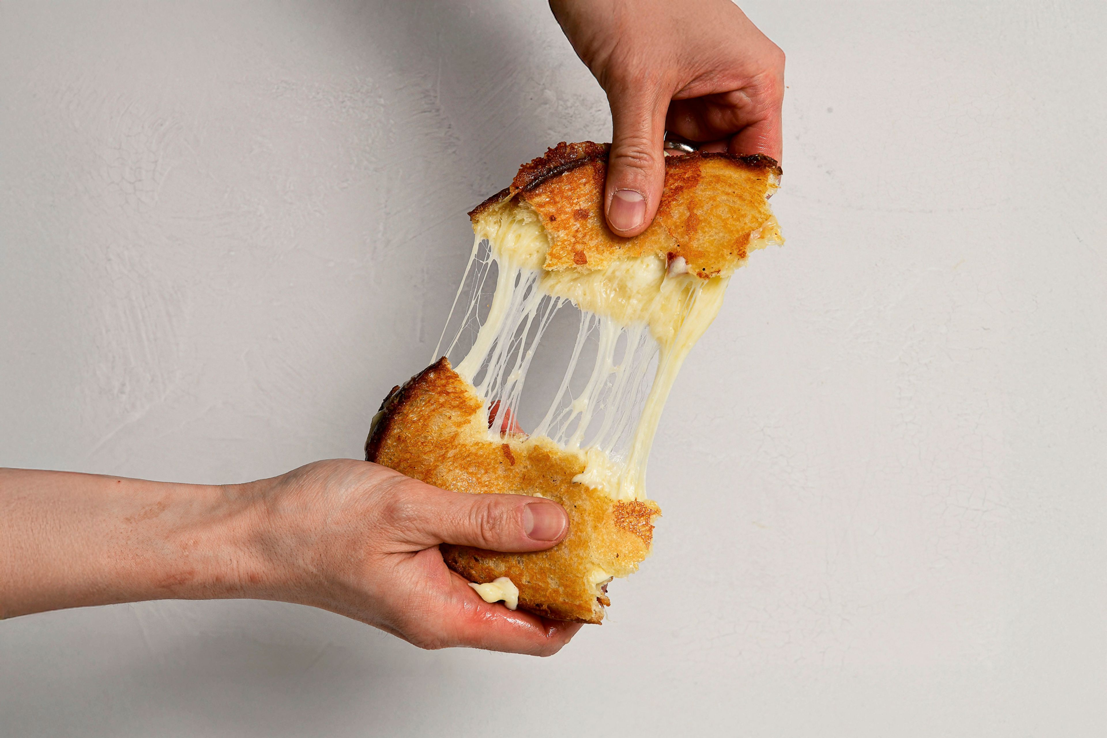 Hands pulling apart a grilled cheese with impressive cheese pull
